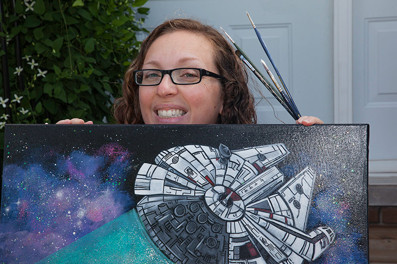 Photo of artist holding a Star Wars painting and paintbrushes